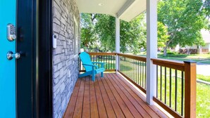 Une terrasse en bois avec un fauteuil Adirondack bleu, un mur en pierre et un plafond blanc.