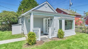 Une petite maison à un étage, dotée d’un porche, d’un garage et avec une maison rouge en arrière-plan.