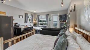 A modern bedroom with a large bed, a desk, a sofa, and a view of the outdoors.
