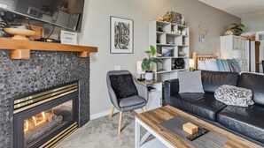 A modern living room with a fireplace, a black leather sofa, a wooden coffee table, and a bookshelf.