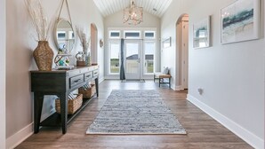 Un couloir avec une console en bois foncé, des paniers en osier, un tapis à motifs et un luminaire suspendu.