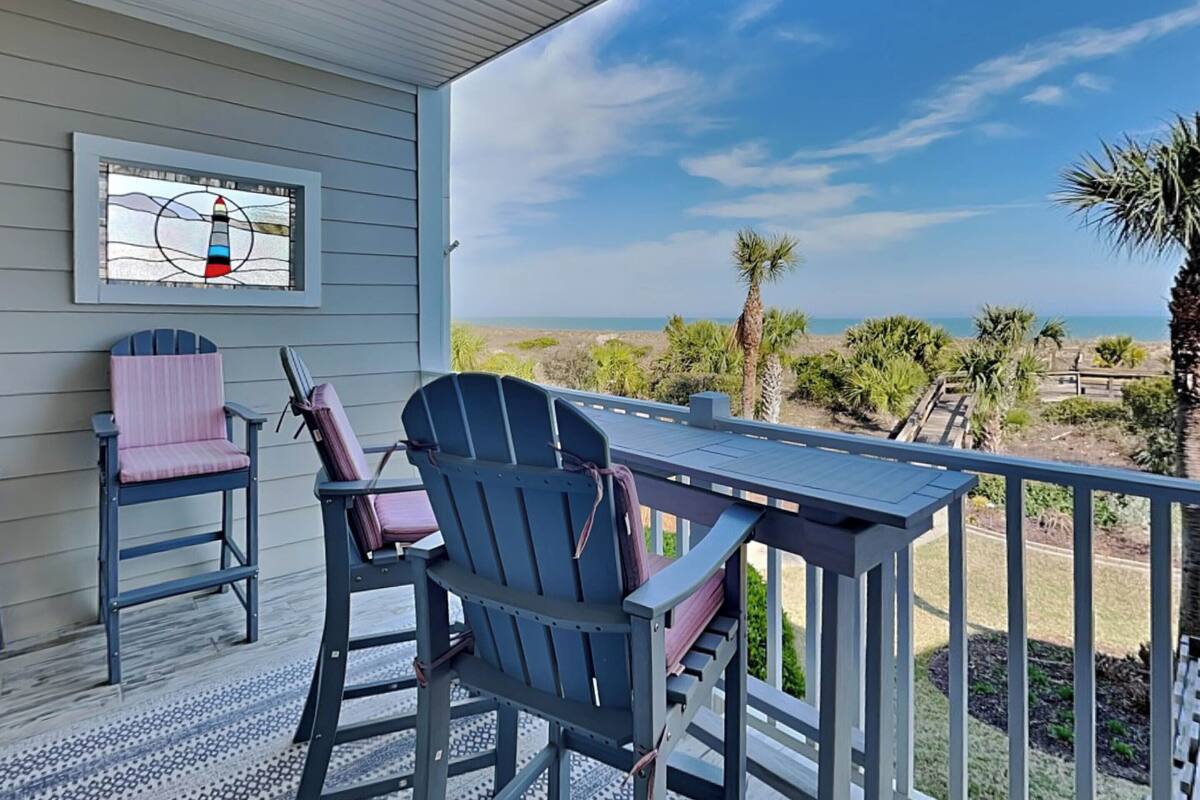 A covered outdoor area with a table and chairs, a view of the beach, and a lighthouse artwork.