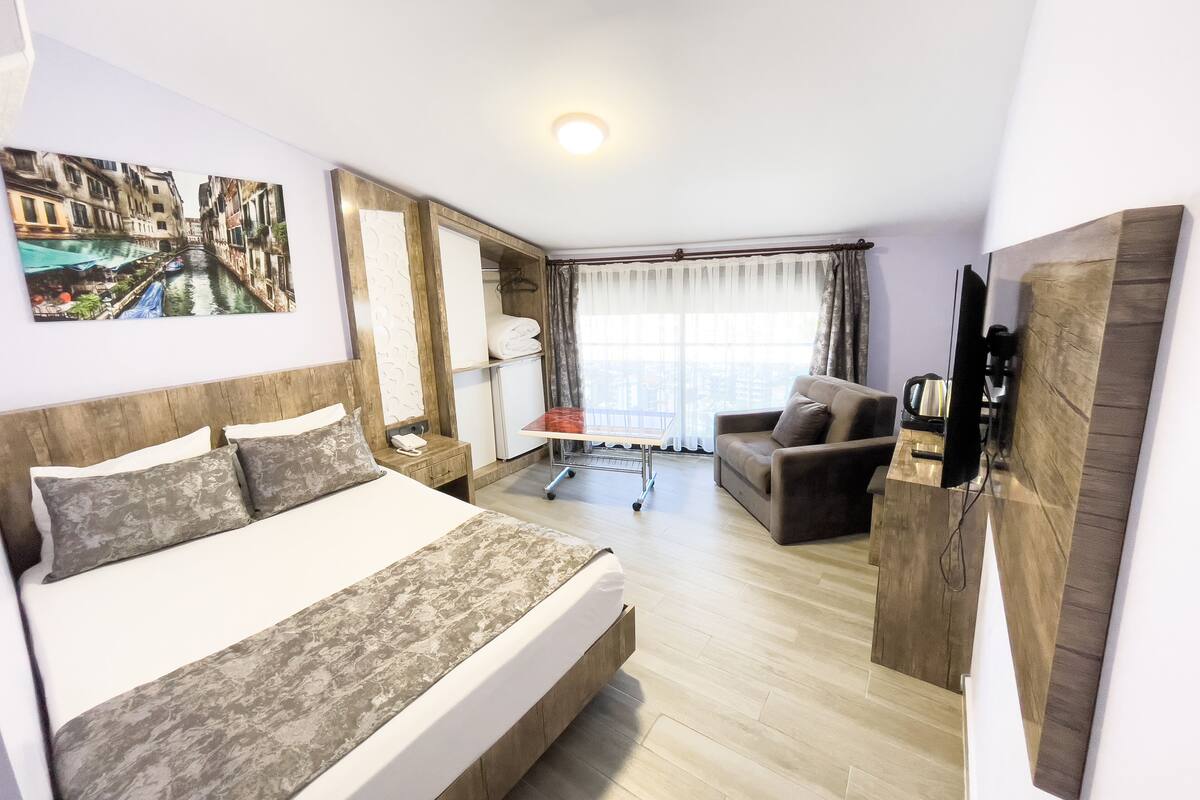 A hotel room with a bed, a sofa, a desk, a TV, and a window with curtains.
