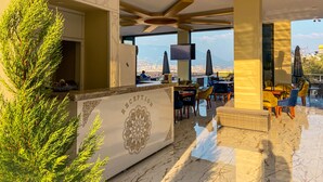 A modern bar area with a view of the city and mountains, featuring a reception desk, seating, and a large TV screen. - Castle's Light Boutique Hotel (Alanya)