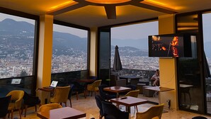 A rooftop restaurant with a city view, tables, chairs, and a TV screen. - Castle's Light Boutique Hotel (Alanya)