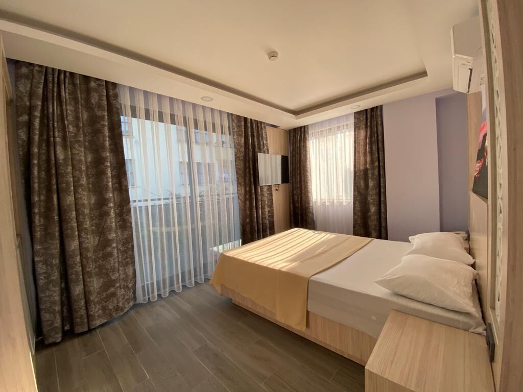 Una habitación de hotel con cama, cortinas, televisión y ventana.