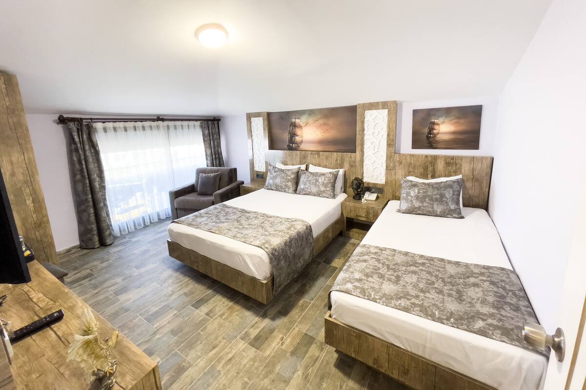 A hotel room with two beds, a sofa, a TV, and a wooden floor.
