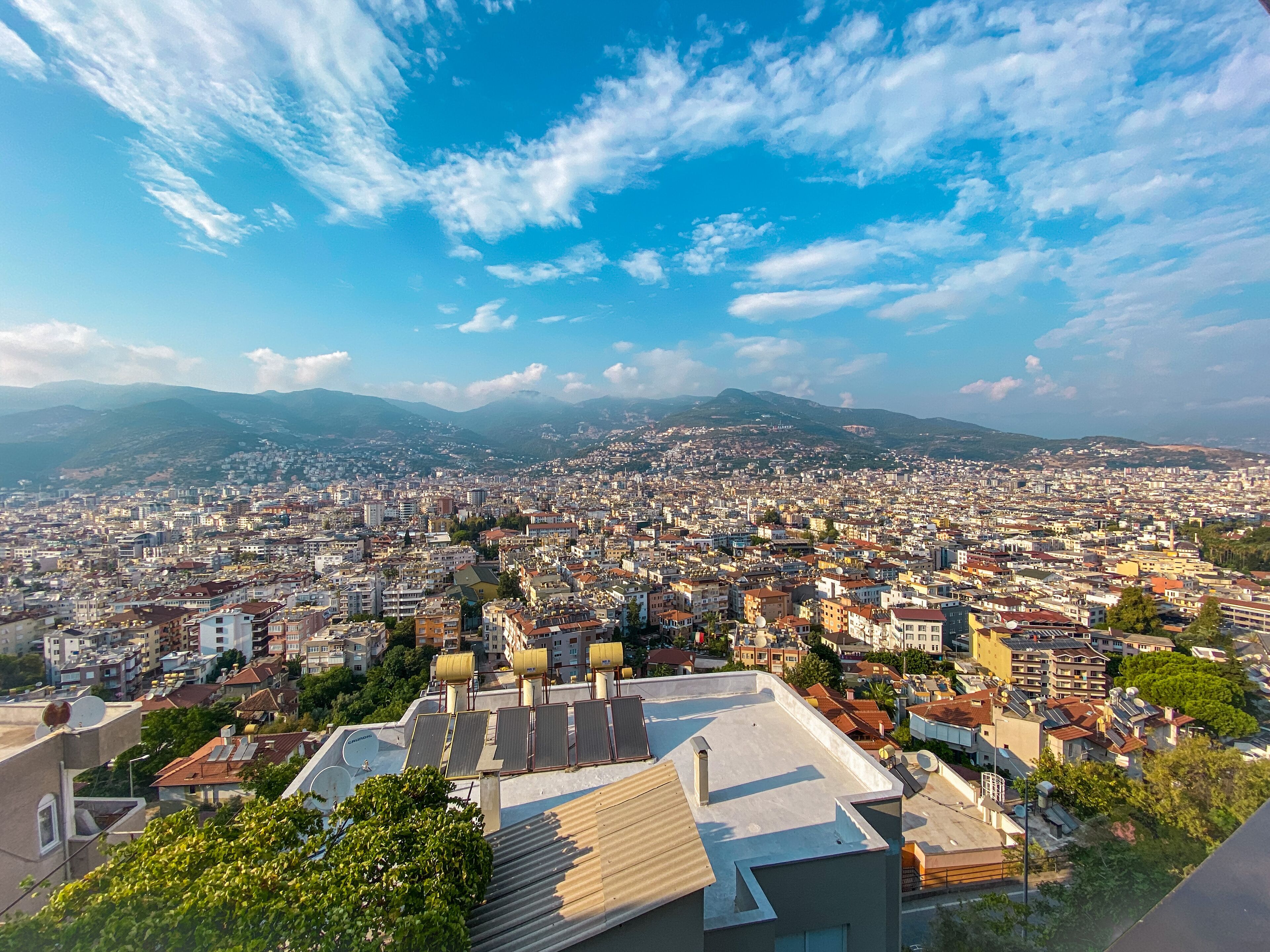 Vista panorámica de un paisaje urbano con edificios residenciales y comerciales, cielo despejado y montañas al fondo.