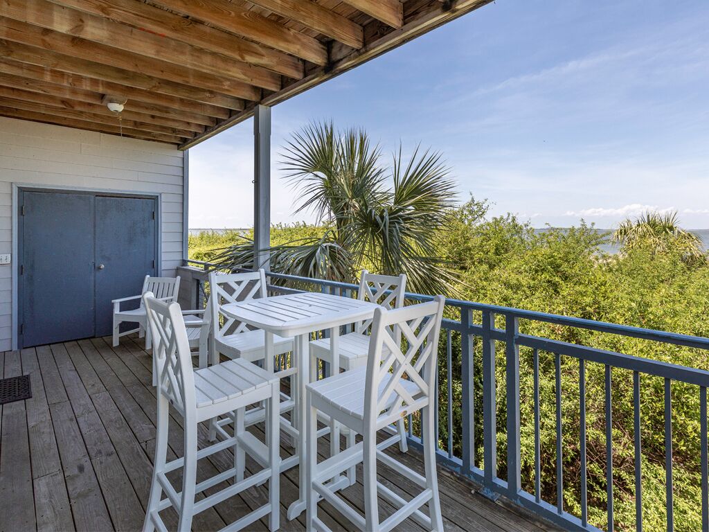 Un espace extérieur abrité doté d’une terrasse en bois, de mobilier blanc et offrant une vue sur la verdure et l’eau.