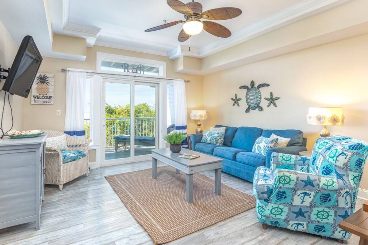 A living room with a blue sofa, a patterned armchair, a coffee table, and a ceiling fan.