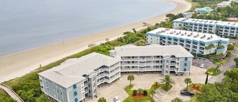 A beachfront hotel with multiple buildings, a parking area, and a view of the ocean.