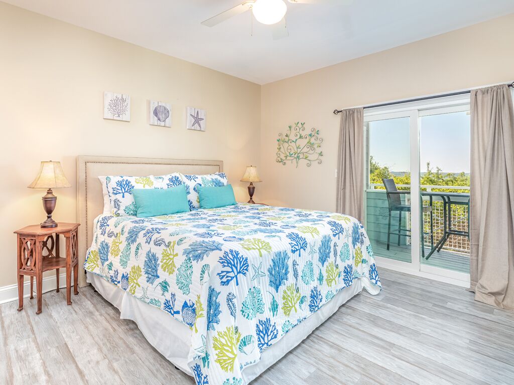 A bedroom with a bed, two bedside lamps, a small wooden table, and a balcony with a glass railing.