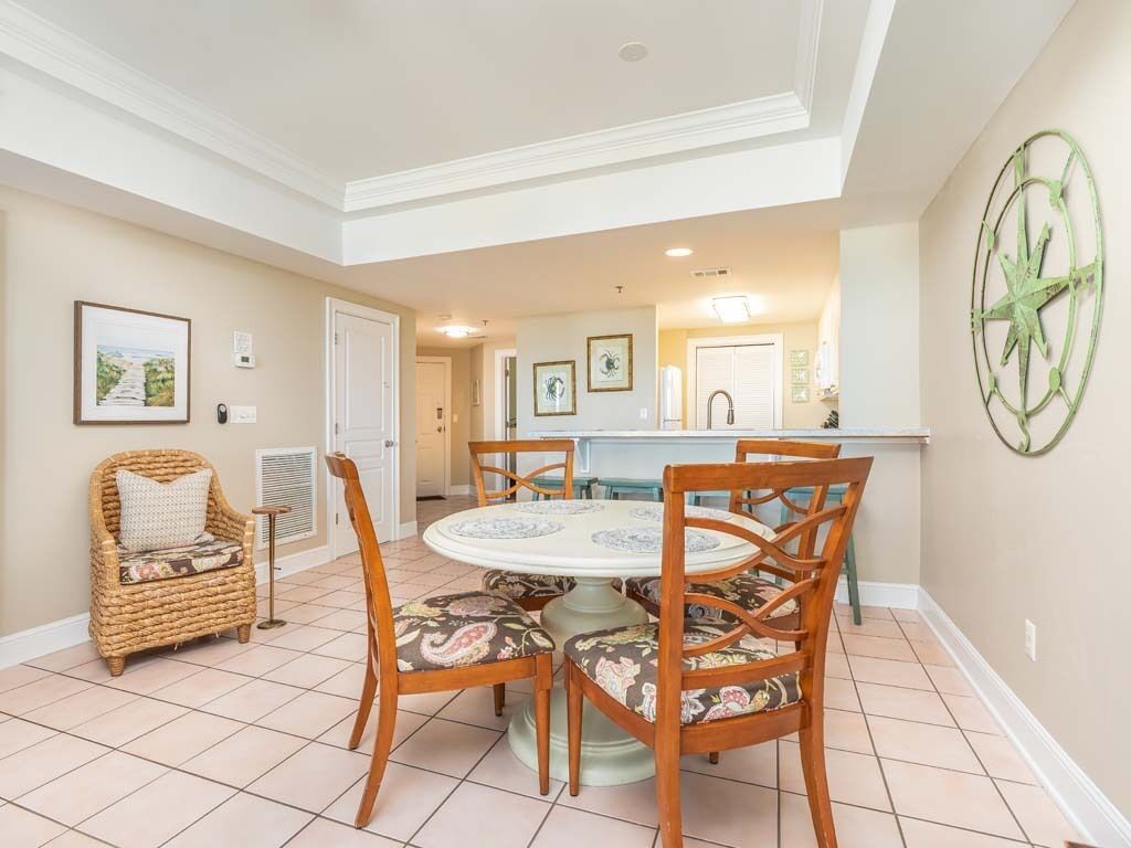 Un coin repas comprenant une table ronde et quatre chaises, un fauteuil en osier et un élément décoratif en forme de boussole fixé au mur.