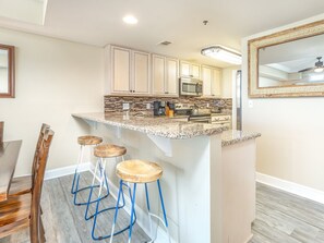 Una cocina con encimera de granito, taburetes de madera y armarios blancos.