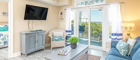 A living room with a sofa, a coffee table, a TV, and a sliding glass door leading to a balcony.