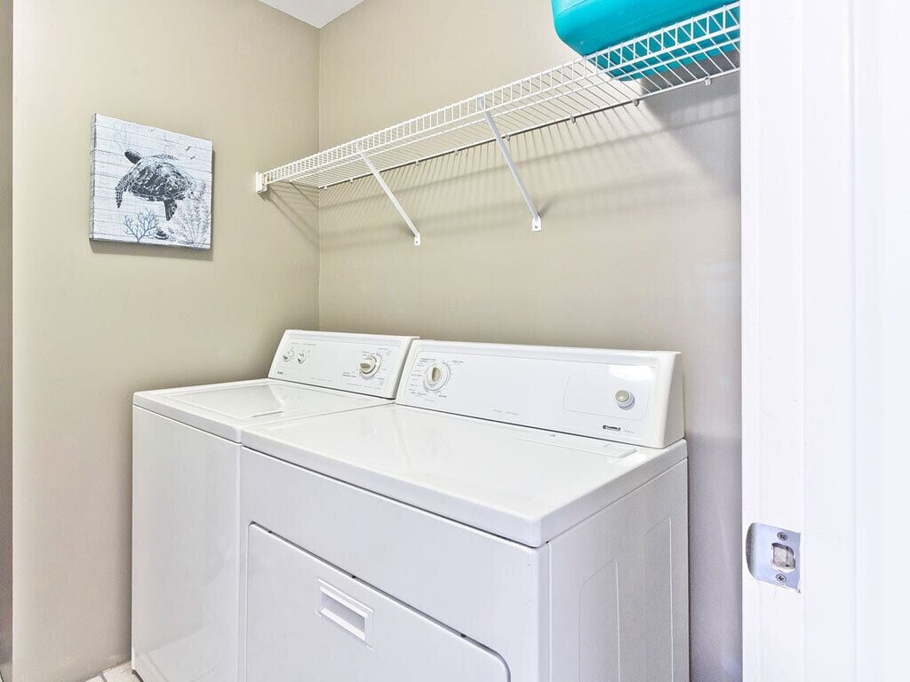 A laundry area with a front-loading washer and dryer, a drying rack, and a framed picture on the wall.