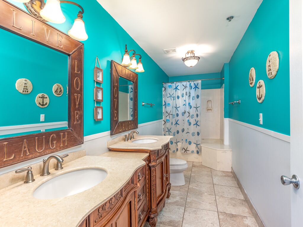 A bathroom with turquoise walls, a wooden vanity with a mirror, two sinks, and a shower curtain with starfish and anchor patterns.