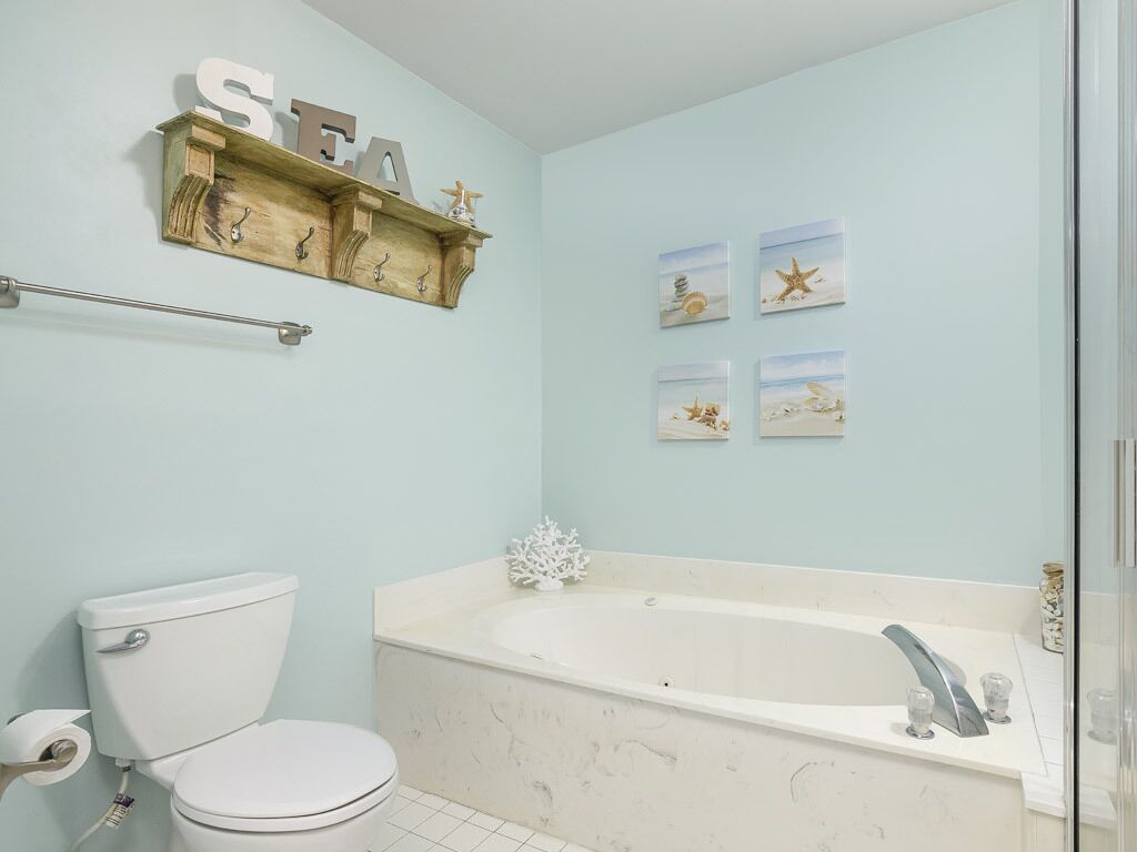 A bathroom with a toilet, a bathtub, a towel rack, and wall art.
