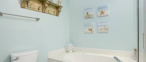 A bathroom with a toilet, a bathtub, a towel rack, and wall art.
