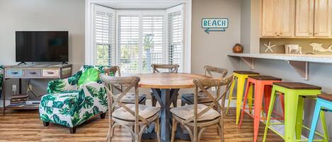 A dining area with a round table and chairs, a television, and a beach-themed sofa.
