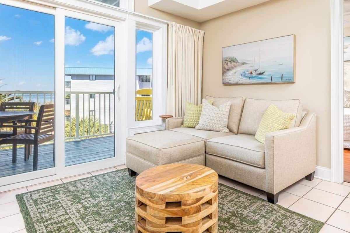 A living room with a beige sofa, a wooden coffee table, and a green patterned rug.