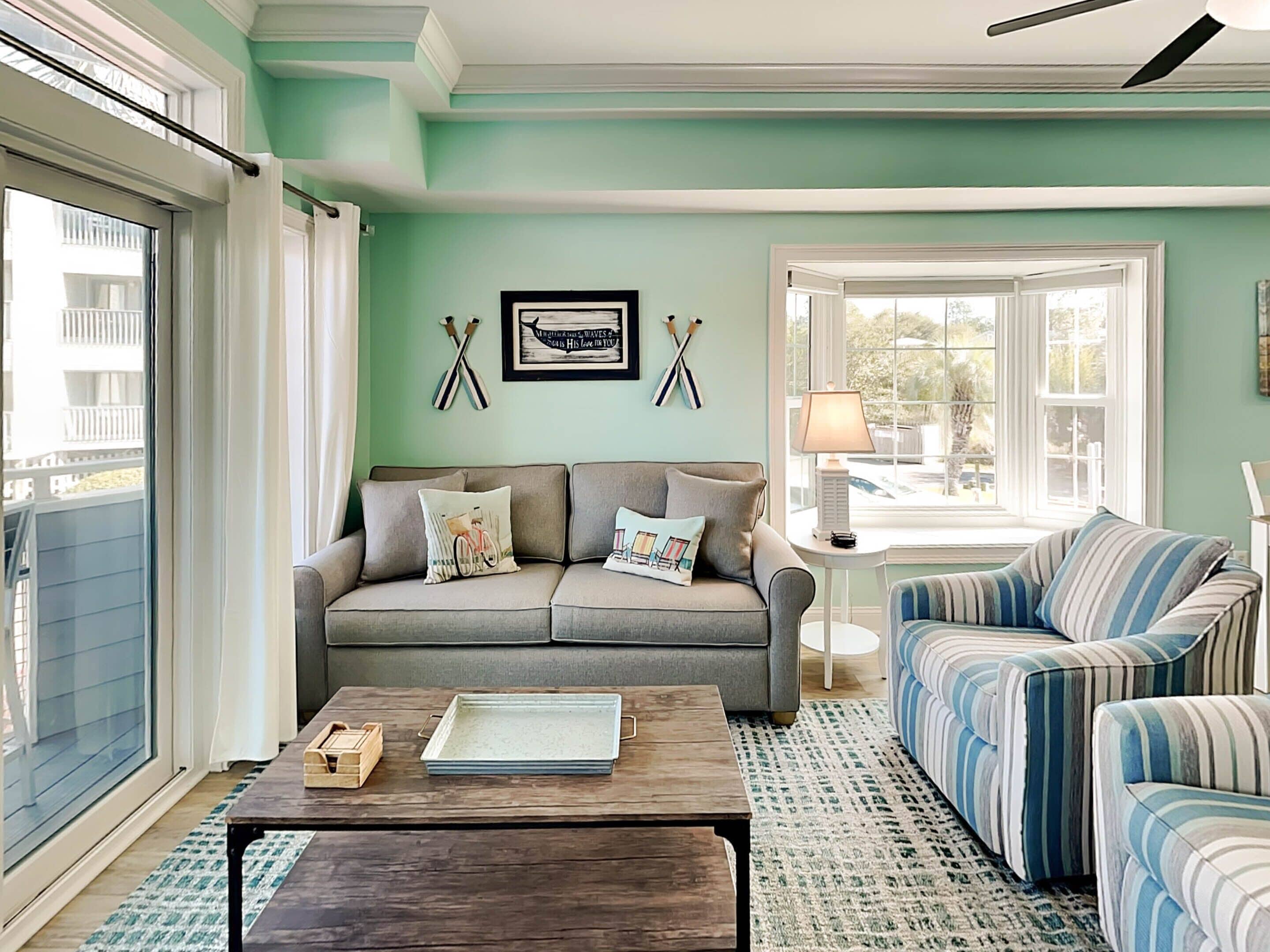 A living room with a sofa, a striped couch, a coffee table, and a window with a view.