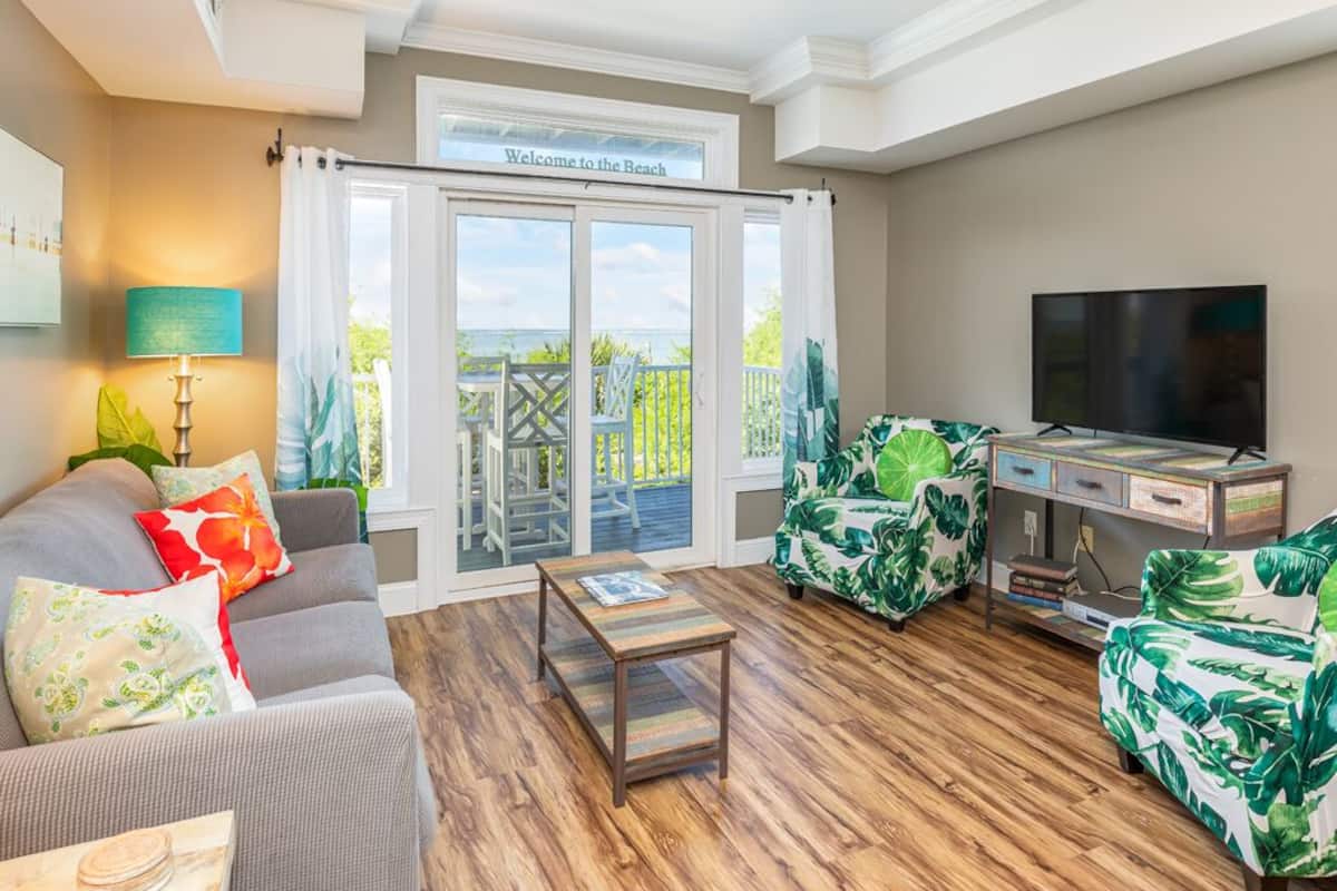 A living room with a grey sofa, a coffee table, a TV stand, and tropical-themed chairs.