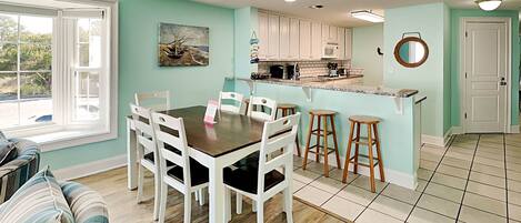 A dining area with a table and chairs, a kitchen with white cabinets, and a sign that reads "BEACH".