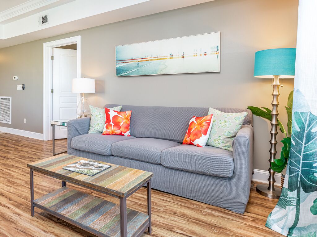 A living room with a grey sofa, colorful pillows, a wooden coffee table, a painting on the wall, and a lamp.