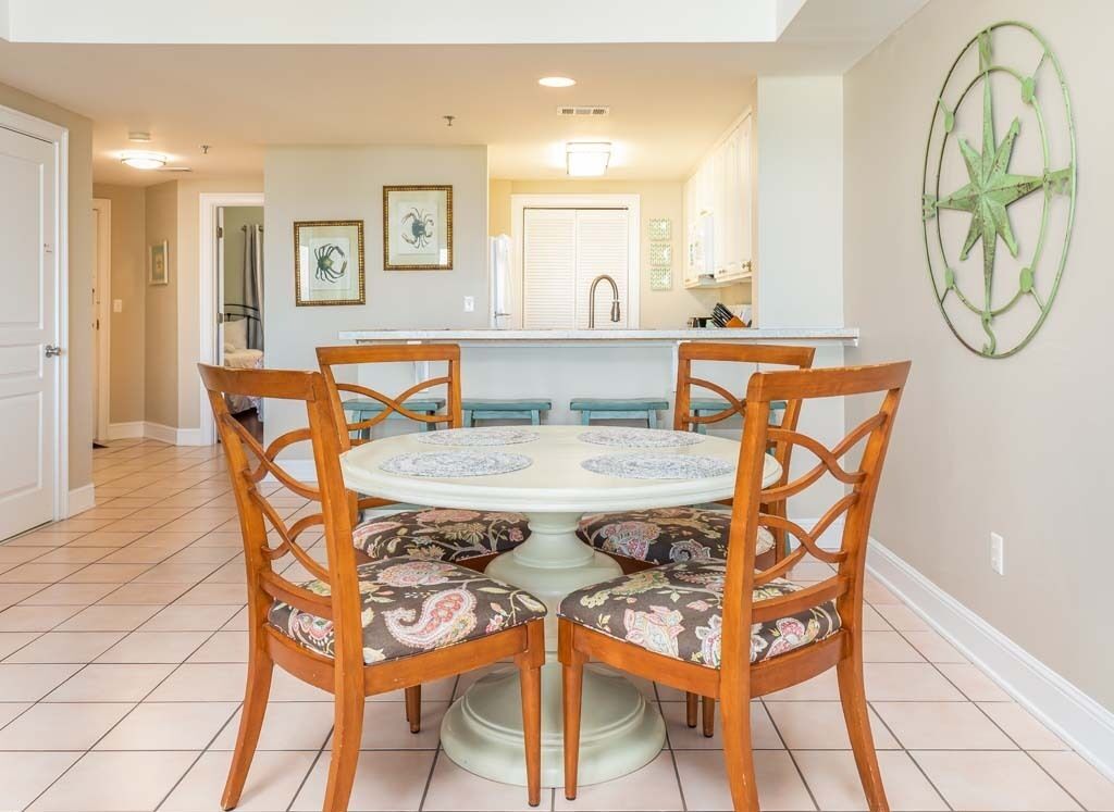 Un comedor con una mesa redonda y seis sillas, una cocina al fondo y una decoración de brújula en la pared.