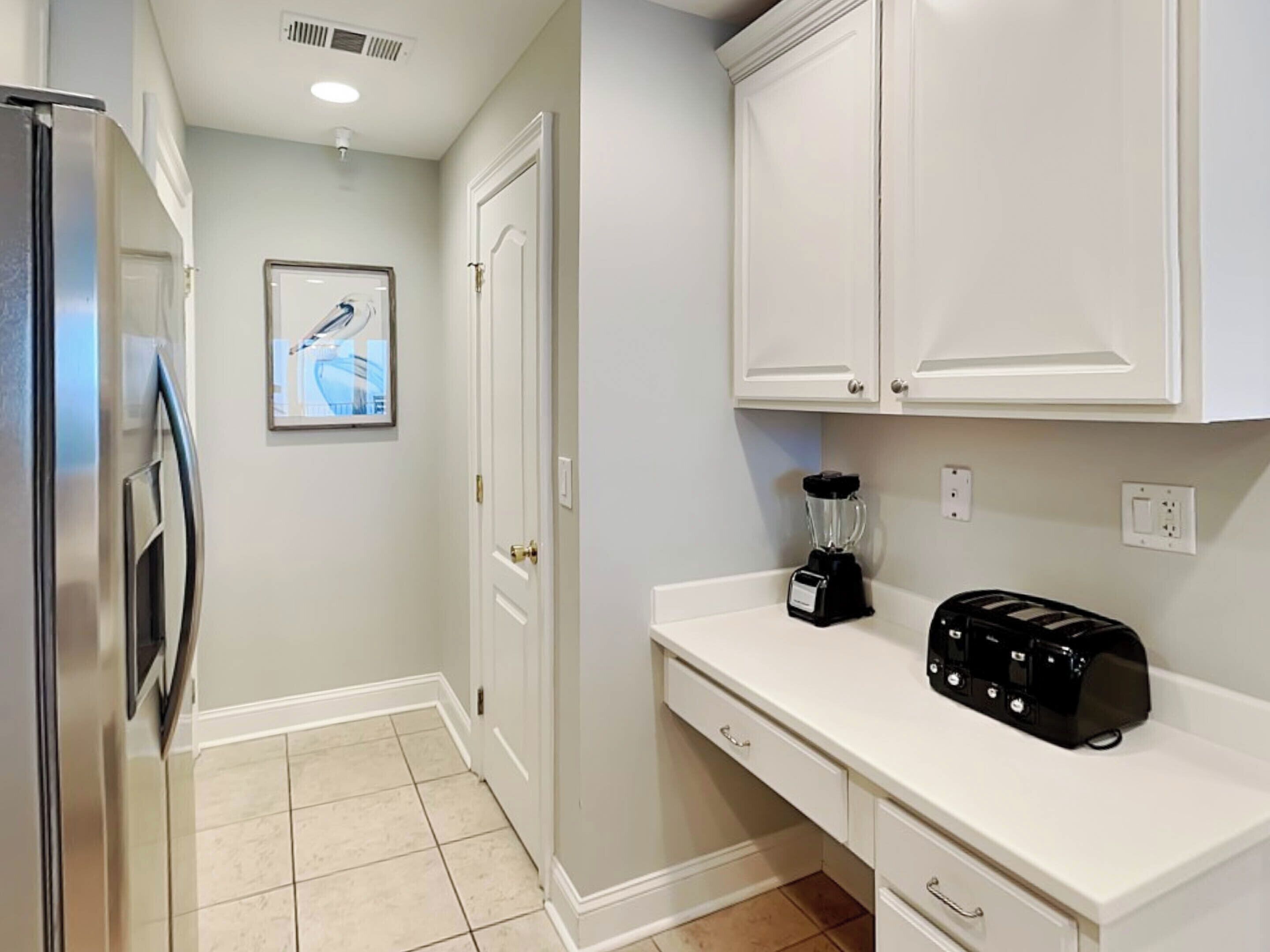 A kitchen with white cabinets, a refrigerator, a toaster, and a blender on the counter.