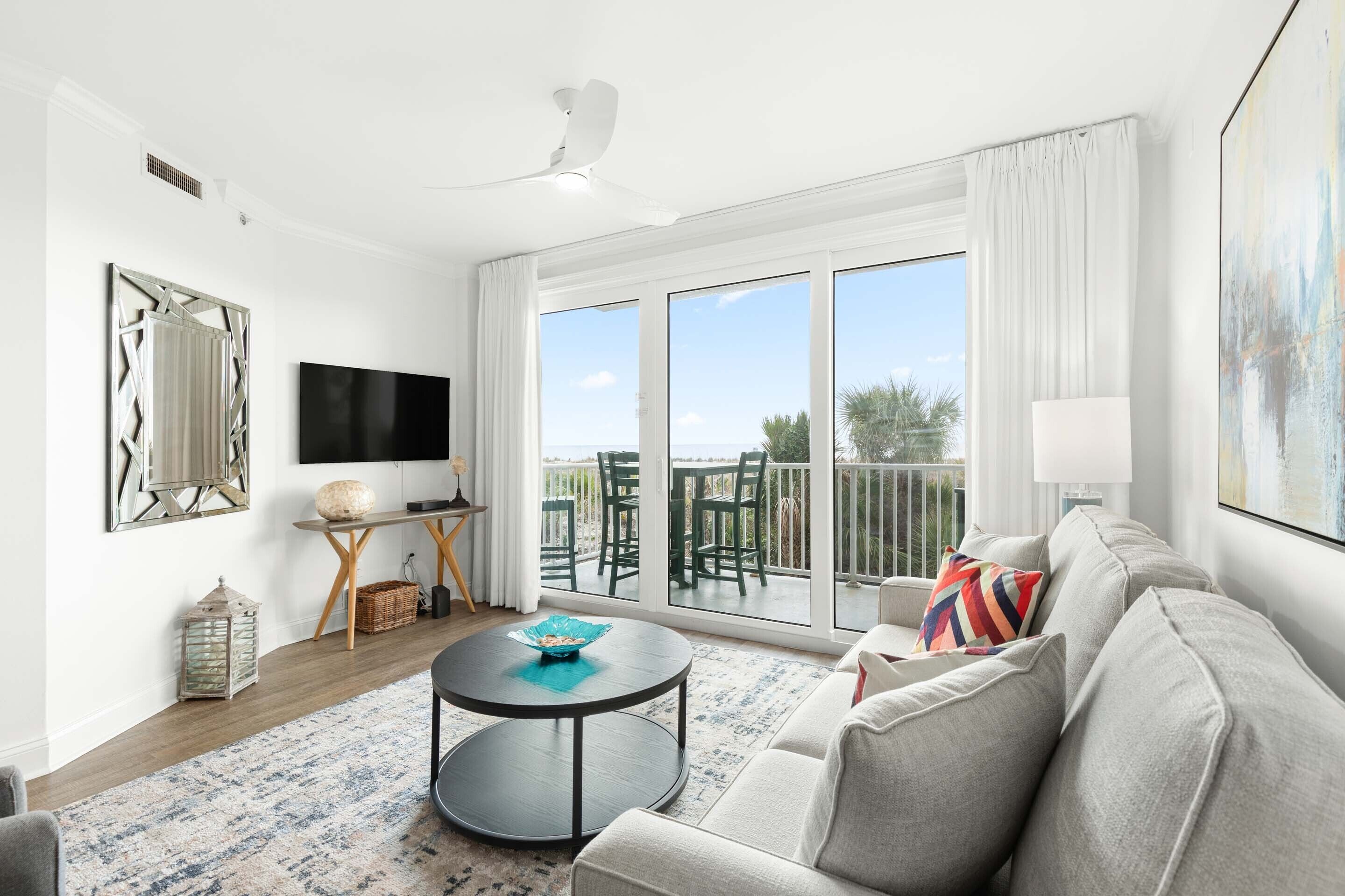 A modern living room with a large TV, a round coffee table, a sofa, and a balcony with outdoor furniture.
