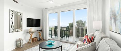 A modern living room with a large TV, a round coffee table, a sofa, and a balcony with outdoor furniture.