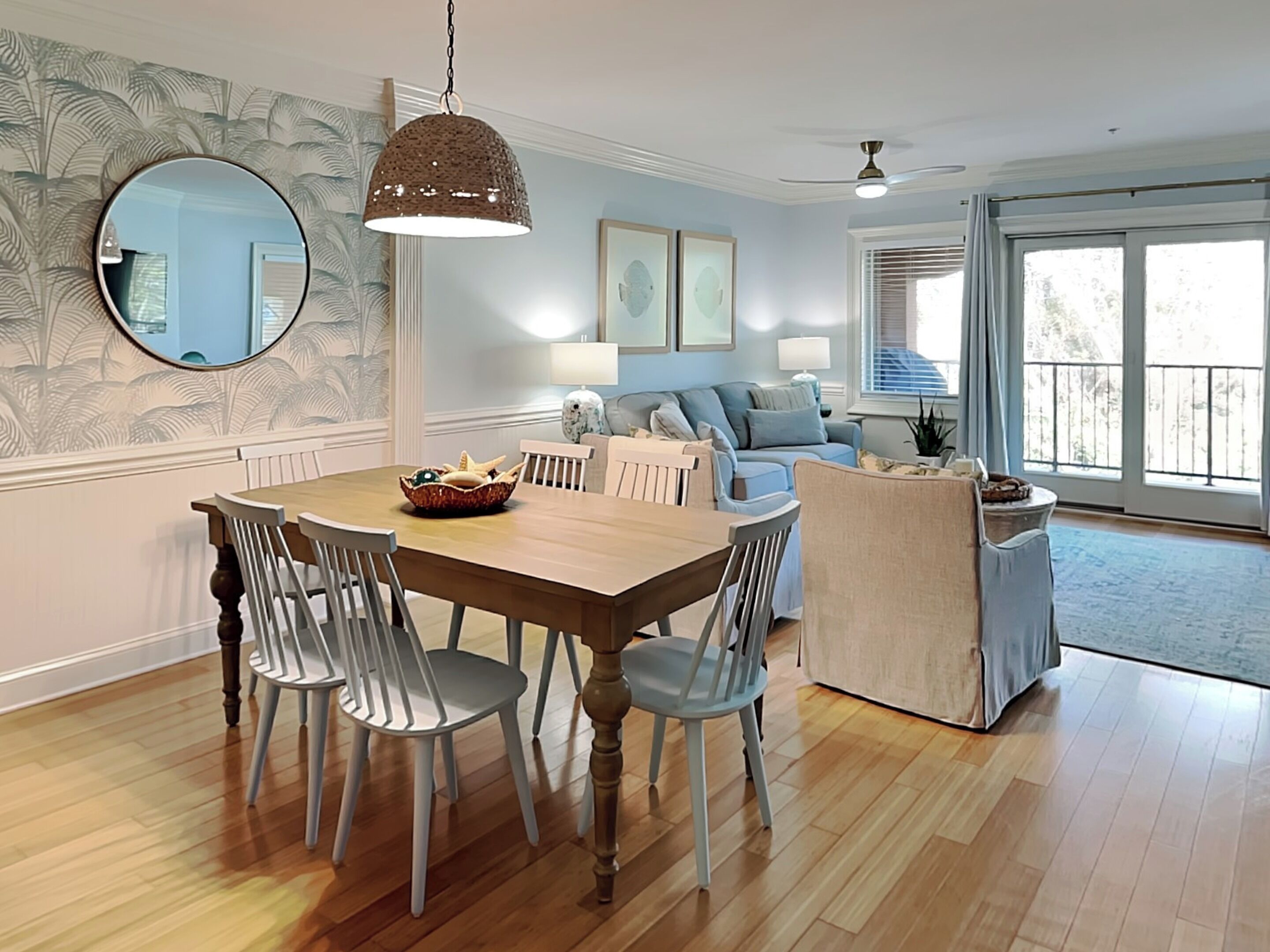 A dining area with a wooden table and chairs, a hanging light fixture, and a large mirror on the wall.