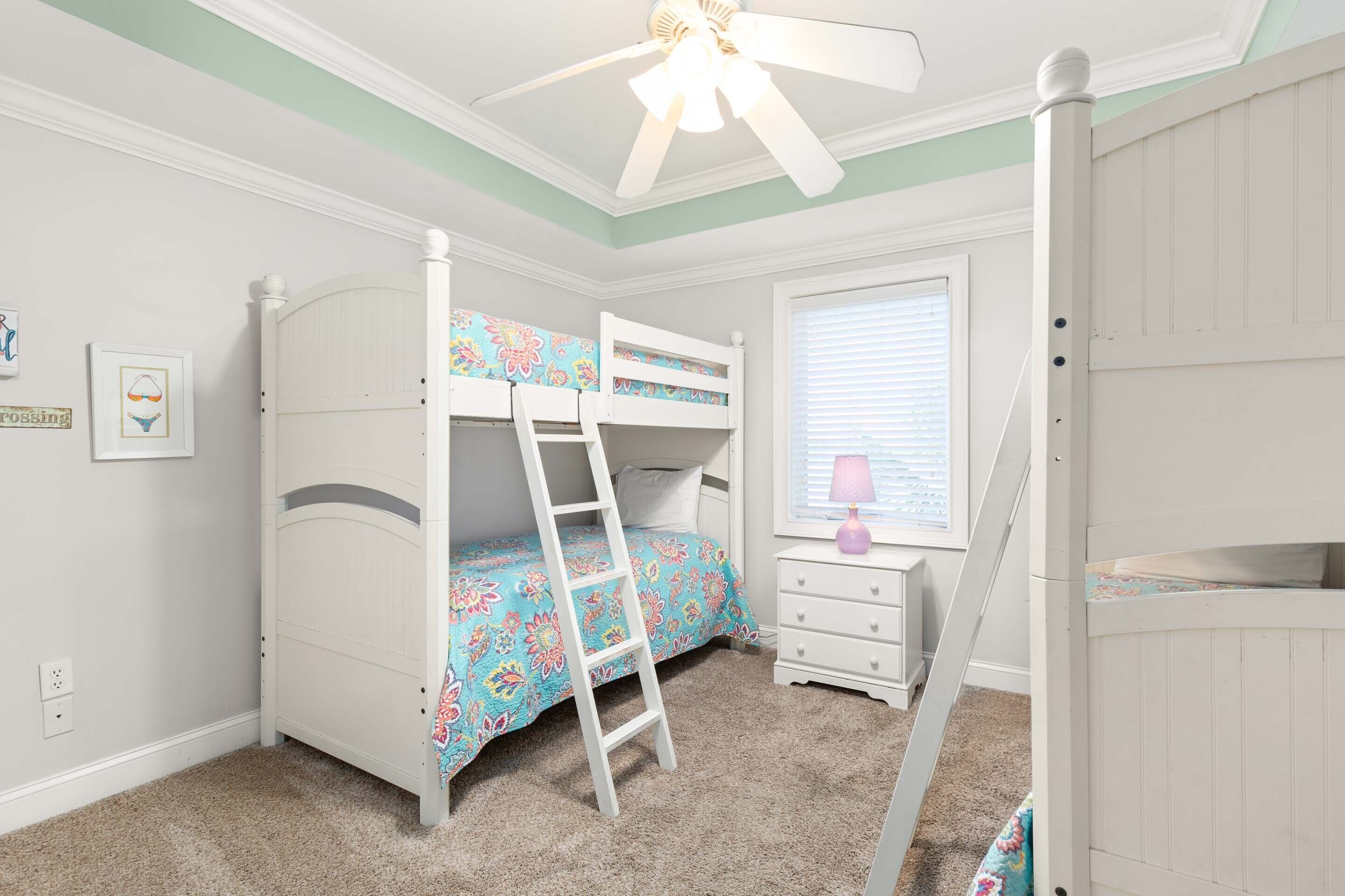 A bedroom with bunk beds, a ladder, a dresser, a window with blinds, and a ceiling fan.