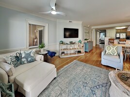 A living room with a white sofa, a blue patterned rug, and a television on the wall.