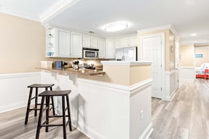Una cocina moderna con armarios blancos, encimera de granito y una isla central con taburetes.