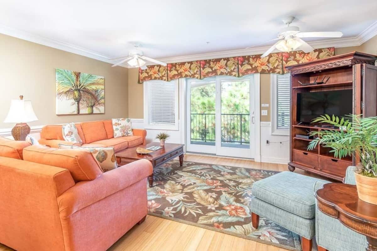 A living room with a sofa, armchairs, a coffee table, a TV stand, and a ceiling fan.