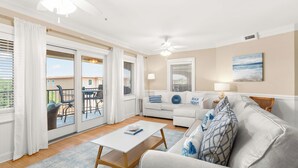 A spacious living room with a white sofa, a coffee table, and a balcony with outdoor furniture. - Brass Rail Villas by Tybee Vacation Rentals (Tybee Island)