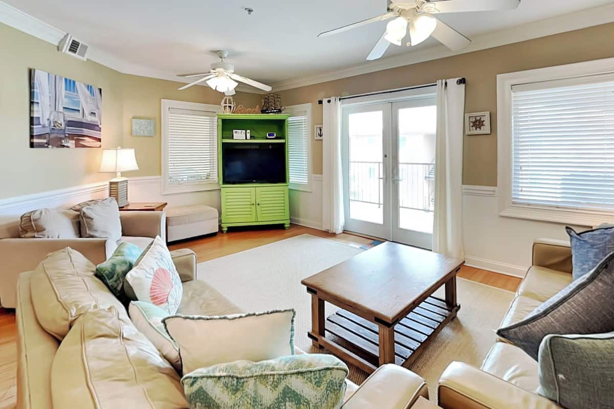 A living room with a green entertainment unit, a beige sofa, a wooden coffee table, and a ceiling fan.