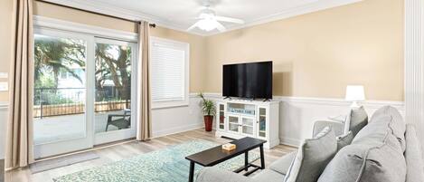 A living room with a sofa, a coffee table, a TV on a cabinet, and a sliding glass door leading to an outdoor area.