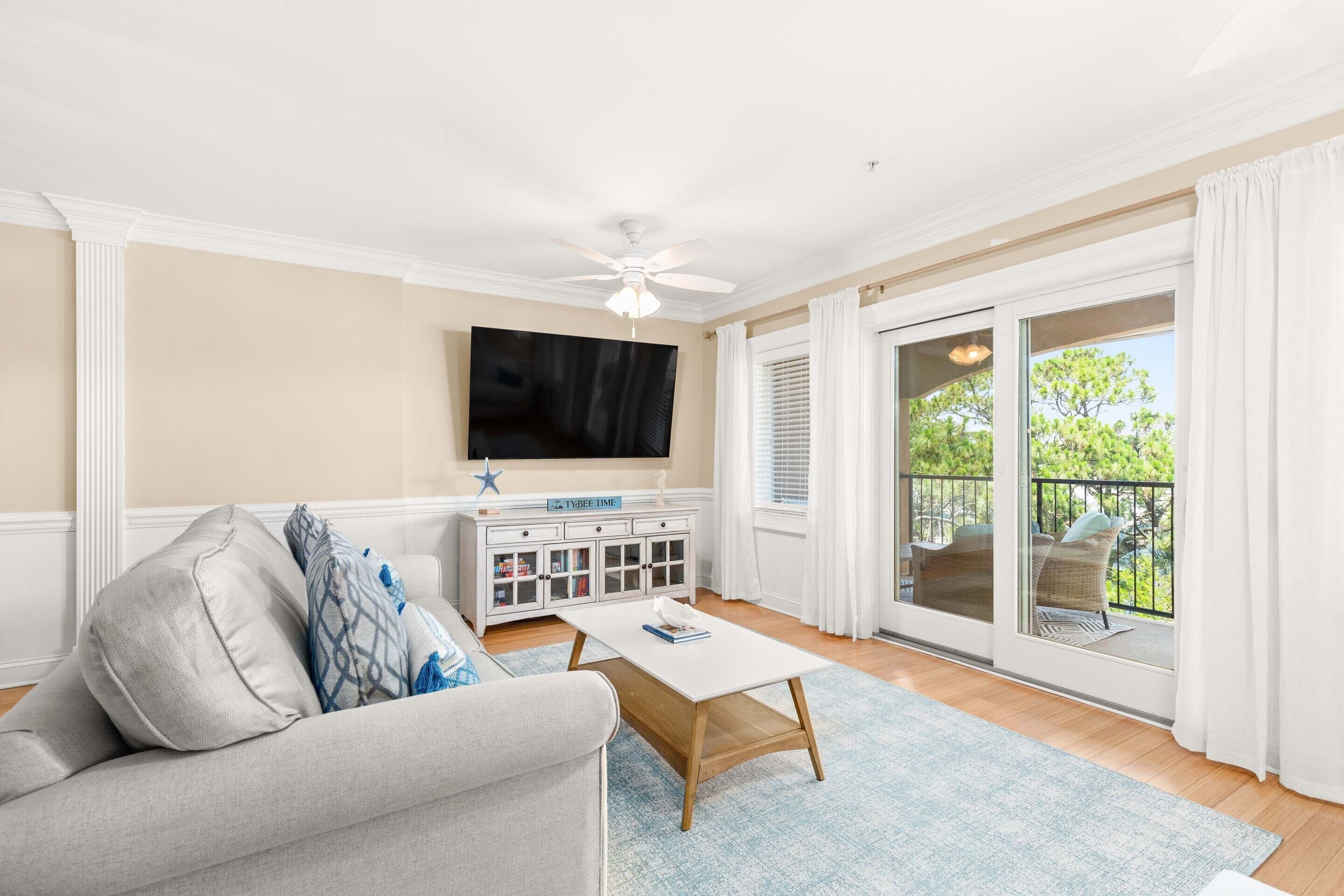 A living room with a sofa, coffee table, TV, and a sliding glass door to a balcony.