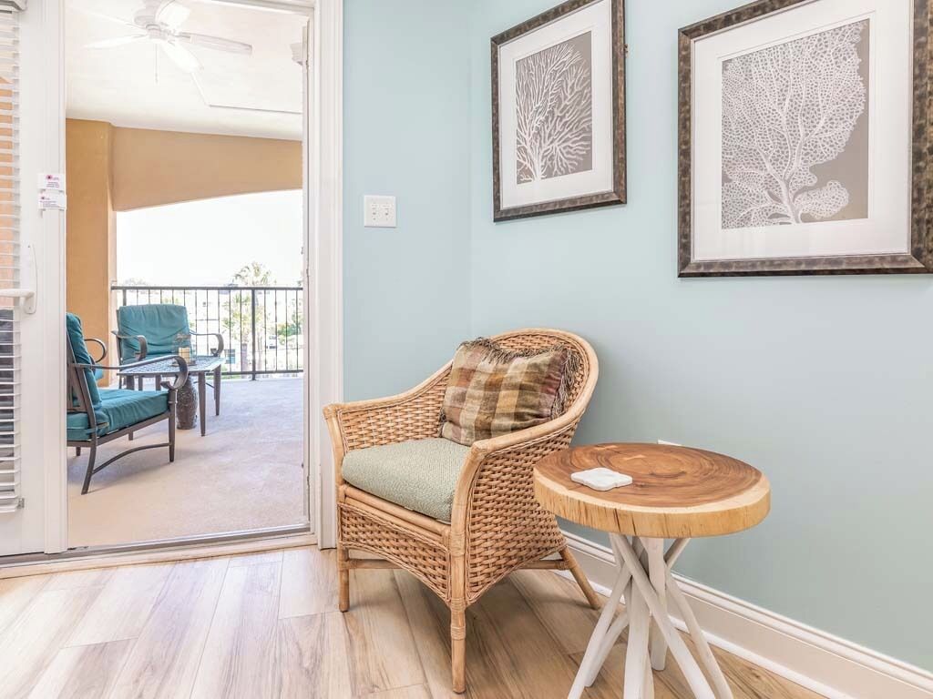 Une pièce comprenant une chaise en osier, une petite table en bois et deux œuvres d’art encadrées accrochées au mur.