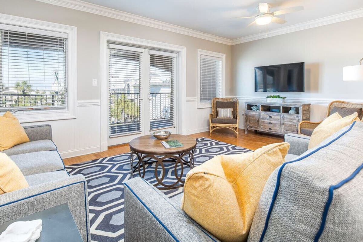 A living room with a sofa set, a coffee table, and a flat-screen TV mounted on the wall.