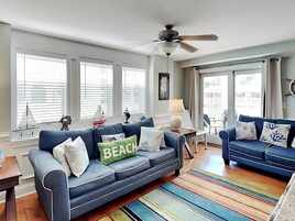 A living room with a blue sofa, a colorful striped rug, and a ceiling fan.