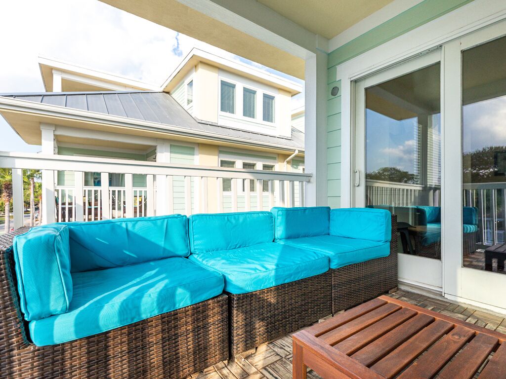 A covered outdoor seating area with a wicker sofa and a wooden table.