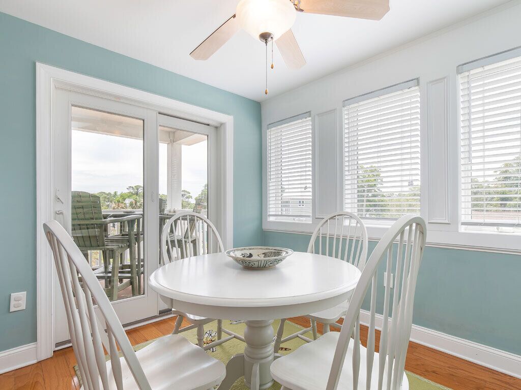 A dining area with a round table, white chairs, and a ceiling fan.