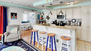 A kitchen with white cabinets, a microwave, and a coffee maker. There are four stools and a chair. - Captains Watch 1 by Tybee Vacation Rentals (Tybee Island)