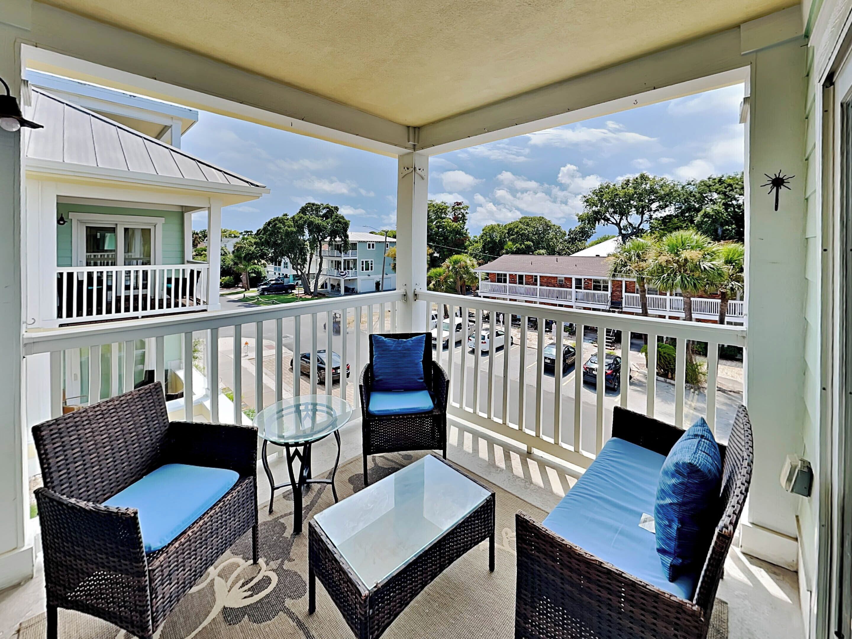 A covered balcony with wicker furniture, a glass table, and a view of the street and buildings.