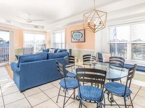 Uma sala de estar moderna com um sofá azul, uma mesa de jantar de vidro com cadeiras, e vista para a cidade através de grandes janelas.